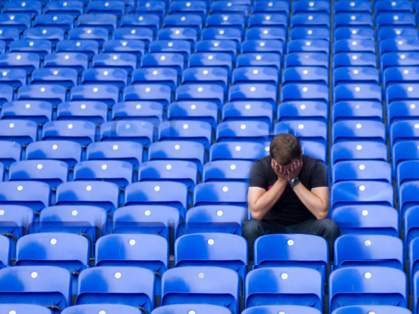Man sitting alone with lots of empty blue seats behind