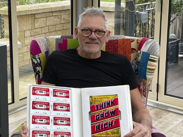 Neville sitting holding mentoring cassette and book