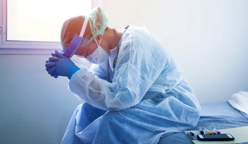 Doctor in scrubs sitting on a bed with his head in his hands