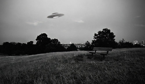 Dish shaped flying Saucer flying over a field with trees in the background